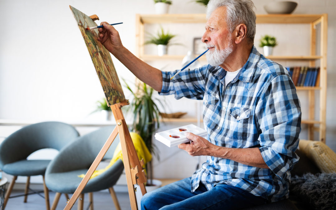 Handsome senior man artist paints on canvas painting on the easel